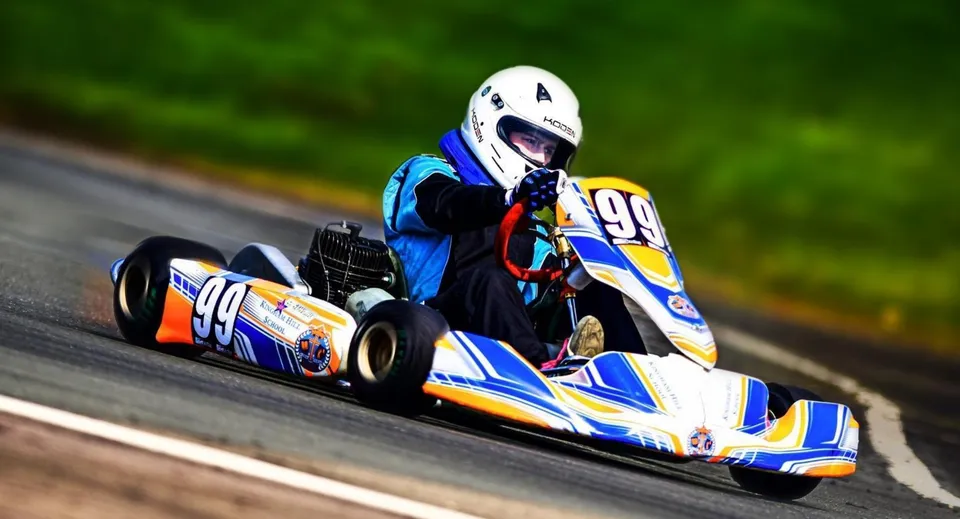 Un pilota con casco guida un kart della Kingham Hill School con il numero 99 su una pista asfaltata.