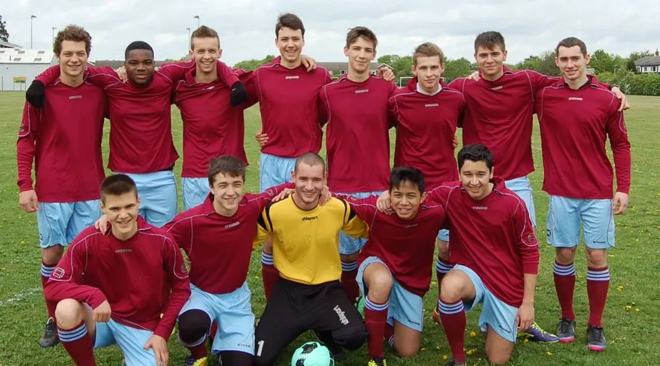 Un gruppo di studenti della CATS Cambridge si trova insieme su un campo da calcio con maglie rosse.
