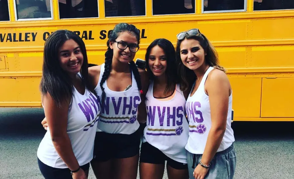 Quattro studentesse della Warwick Valley High School posano davanti a uno scuolabus giallo.