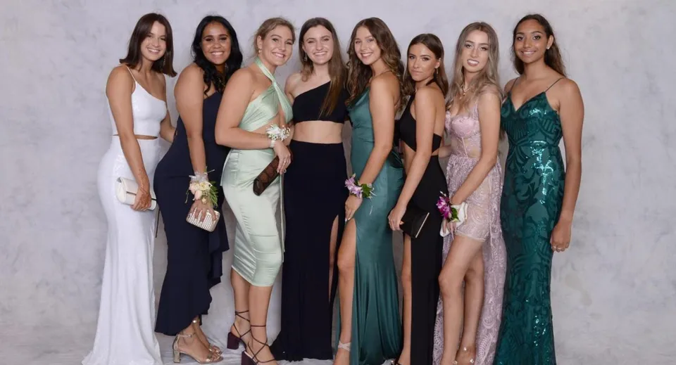 Un gruppo di studentesse della Assumption Grammar School posa in abito da sera davanti a uno sfondo bianco.