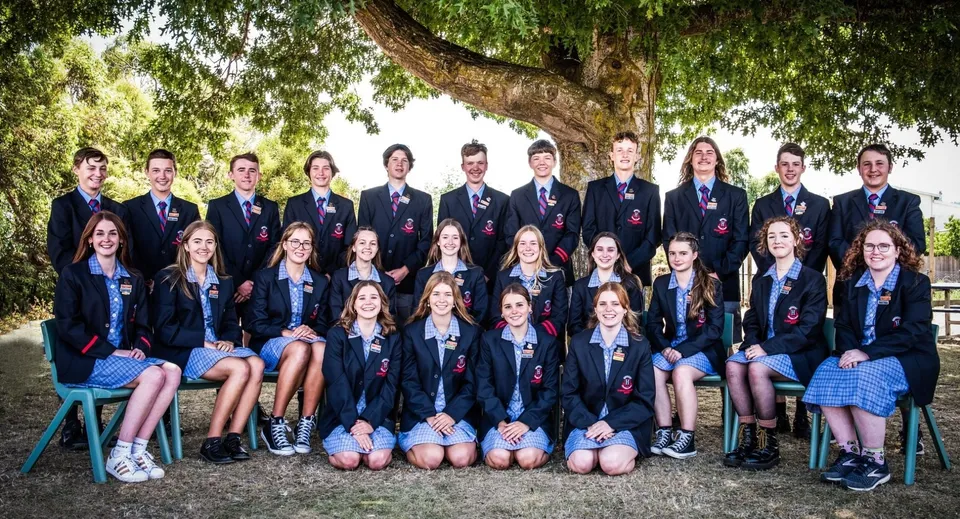 Un gruppo di studenti della Queechy High School si trova insieme sotto un grande albero in un'area simile a un parco.