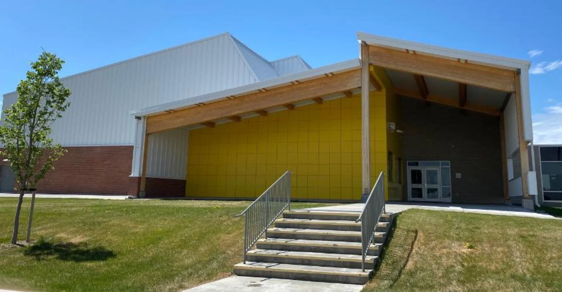 L'edificio moderno a più piani della Huntsville School con facciata gialla e ingresso coperto, circondato da un'area verde e alberi.