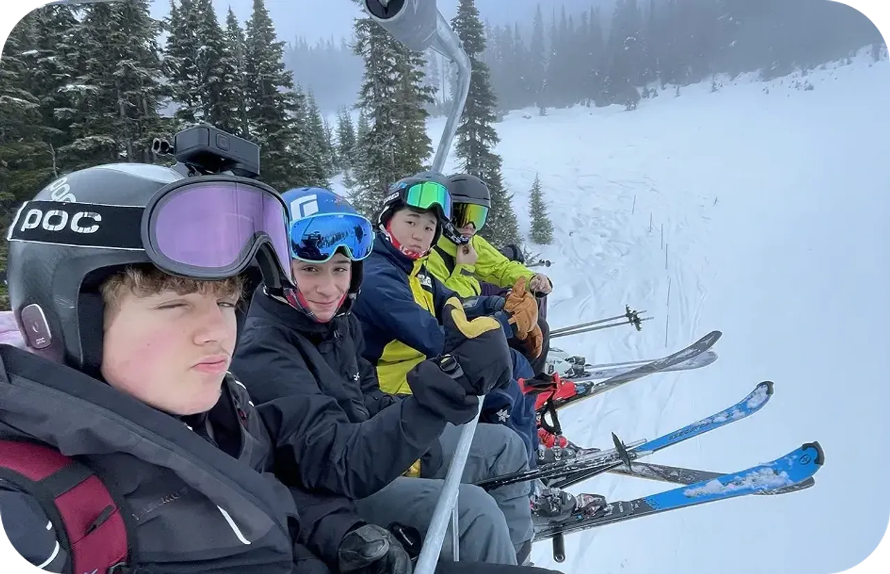 Quattro ragazzi con casco e sci su una seggiovia lungo un pendio innevato