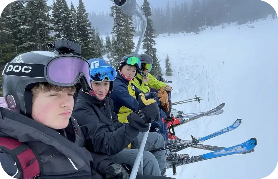 Quattro ragazzi con casco e sci su una seggiovia lungo un pendio innevato