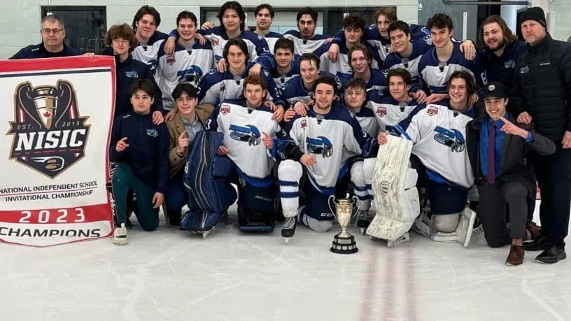 El equipo de hockey de la École secondaire publique Le Sommet posa con un trofeo y una pancarta tras ganar el campeonato.