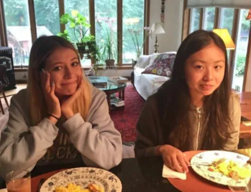 Dos jóvenes sonriendo sentadas a la mesa comiendo frente a grandes ventanales en un salón