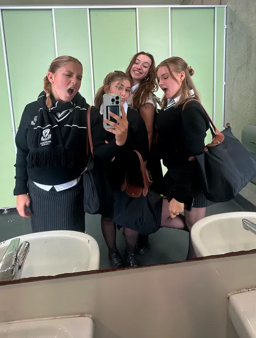 Cuatro estudiantes con uniforme escolar se hacen un selfie ante el espejo del baño del instituto
