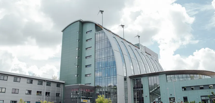 L'edificio moderno di The Sheffield College con facciata in vetro e turbine eoliche sul tetto sotto un cielo nuvoloso.
