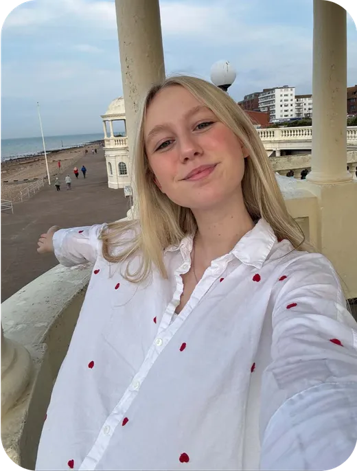Estudiante se hace un selfie en el paseo marítimo con la playa y una columnata al fondo
