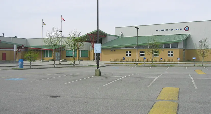 L'edificio a più piani con tetto verde e facciata gialla della J.N. Burnett Secondary School è circondato da un parcheggio.