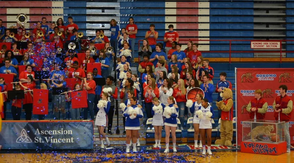 Un gruppo di studenti in uniformi rosse e blu è in piedi nella palestra della Kokomo-Center Township Consolidated School Corporation.