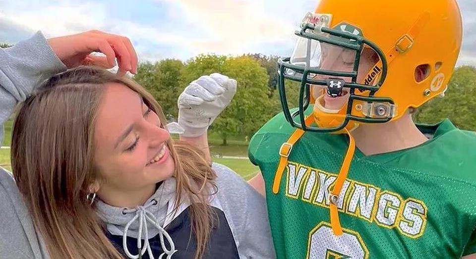 Una persona con la maglia sportiva verde dei Vikings si trova accanto a un'altra persona nel terreno del Barrie North Collegiate Institute.