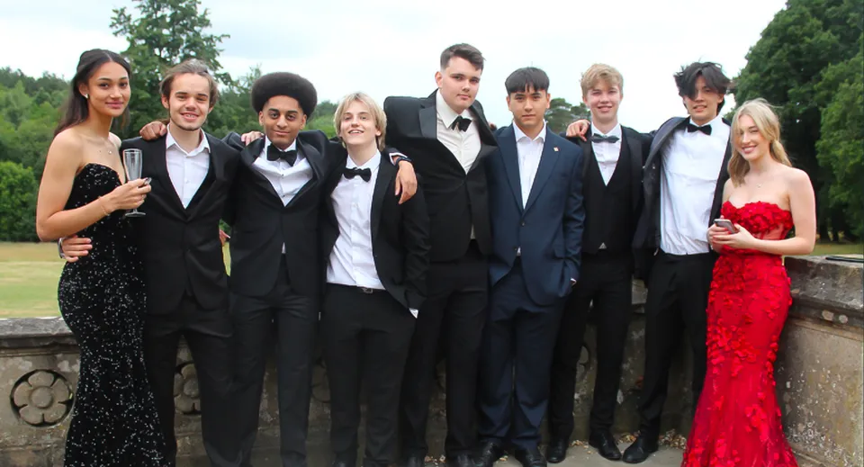 Un gruppo di persone in abito formale posa nel verde del campus di Reddam House Berkshire.