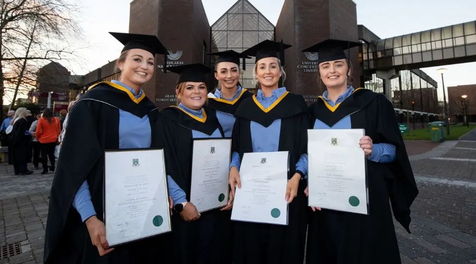 Un gruppo di cinque laureati e laureate della University of Limerick sta davanti all'edificio universitario tenendo con orgoglio i propri diplomi.