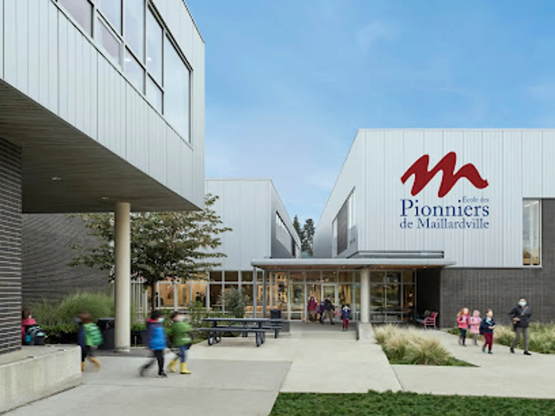 L'edificio moderno in vetro della Pioneer School Port Coquitlam con il logo M mostra persone sul marciapiede antistante.