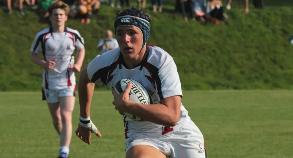 Un giocatore di rugby della Truro School corre con la palla su un campo da gioco.