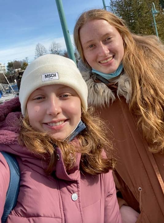 Zwei lächelnde junge Frauen in Winterjacken machen ein Selfie im Freien
