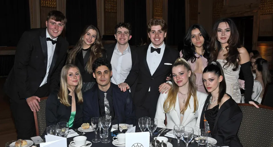 Studenti e studentesse del DLD College London partecipano a una cena formale presso un tavolo elegantemente apparecchiato.