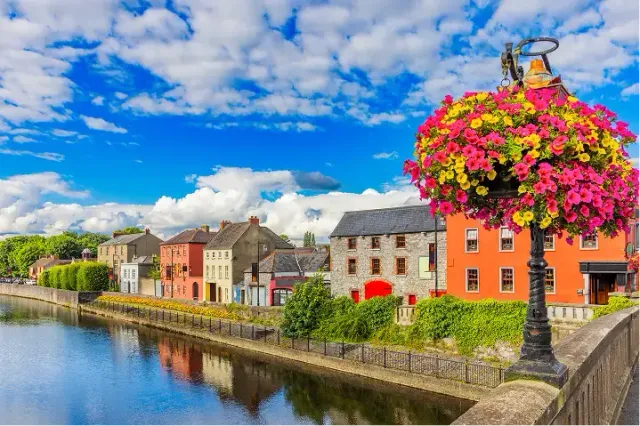 Case colorate lungo un fiume in Irlanda con un cesto di fiori su un lampione