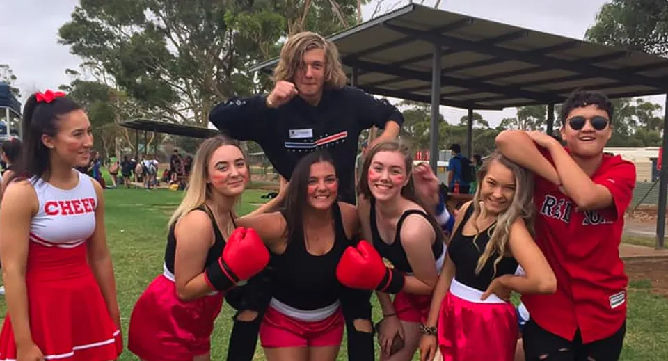 Un gruppo di studenti del Gawler and District College posa insieme all'aperto in un'area simile a un parco, alcuni indossano divise da cheerleader.