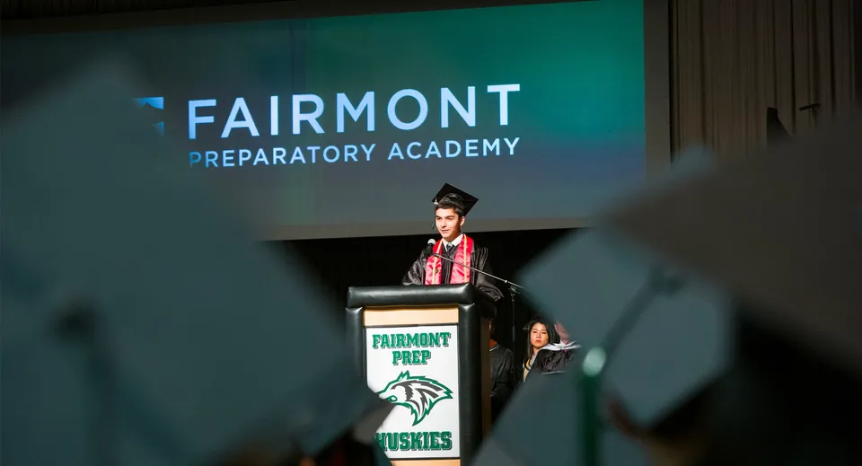 Una persona tiene un discorso al leggio davanti a uno schermo con il logo della Fairmont Prep Academy.