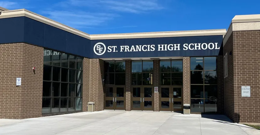 L'edificio in mattoni della St. Francis High School con ampie finestre e l'insegna della scuola sotto un cielo blu.