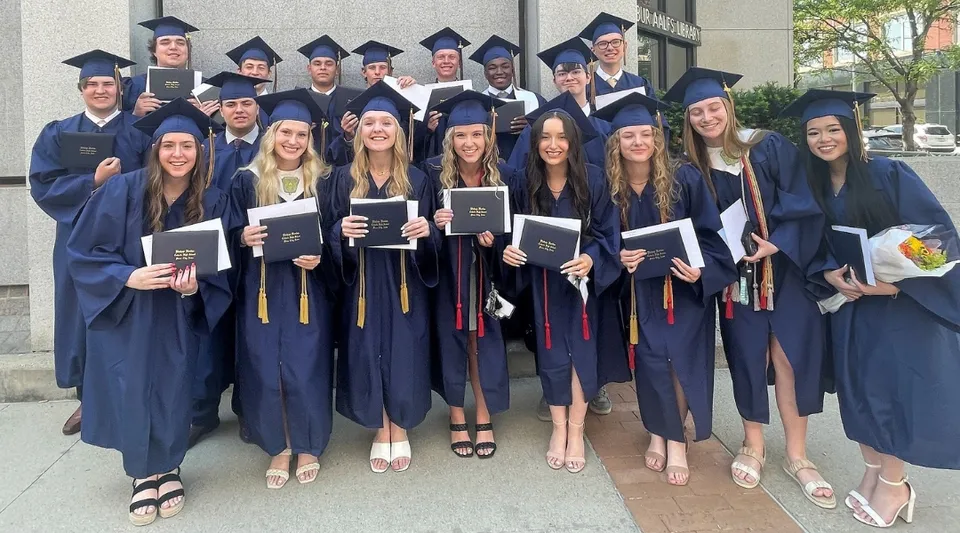 Un gruppo di diplomati della Bishop Heelan Catholic High School è all'aperto in abito accademico e tiene in mano i propri diplomi.