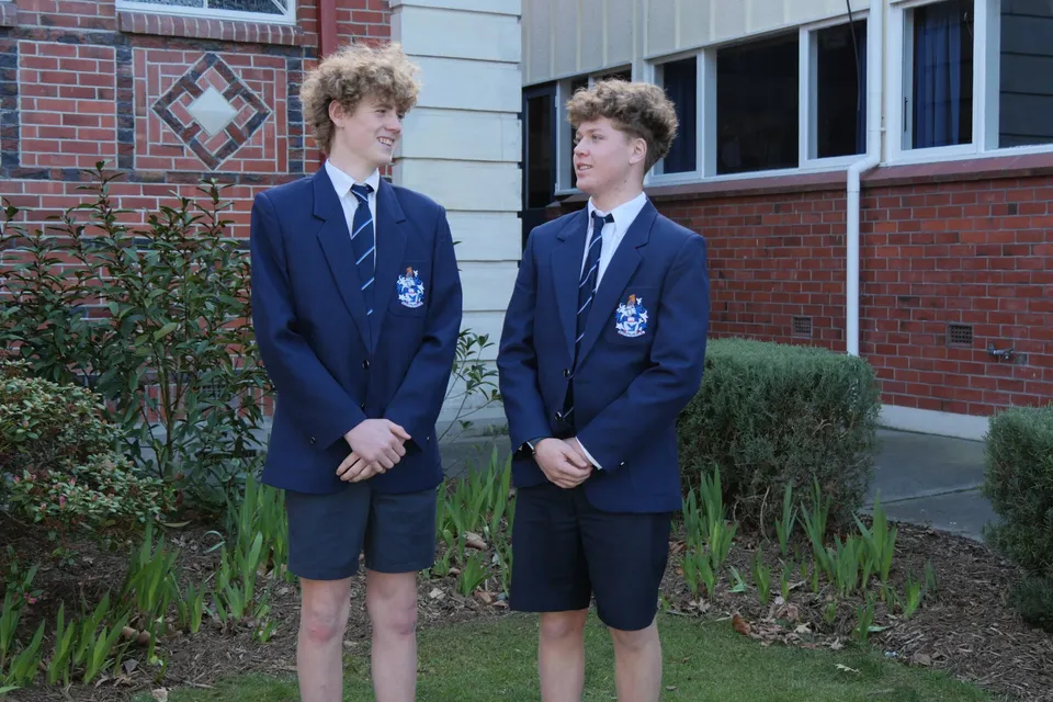 Due studenti della Timaru Boys School si trovano davanti a un edificio in mattoni con finestre a forma di diamante.