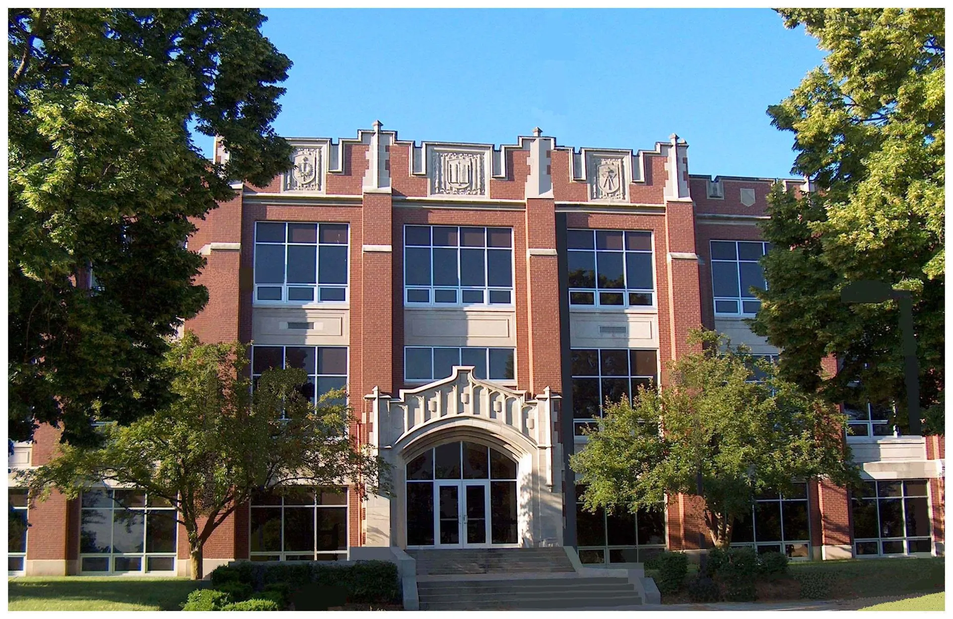 Il grande edificio in mattoni con finestre ad arco della Kokomo High School si trova circondato da alberi e spazi verdi.