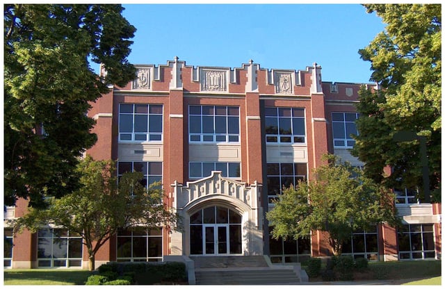 Il grande edificio in mattoni con finestre ad arco della Kokomo High School si trova circondato da alberi e spazi verdi.
