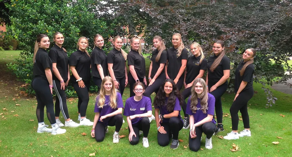 Un gruppo di giovani donne in outfit neri si trova nel verde del campus del Baxter College.
