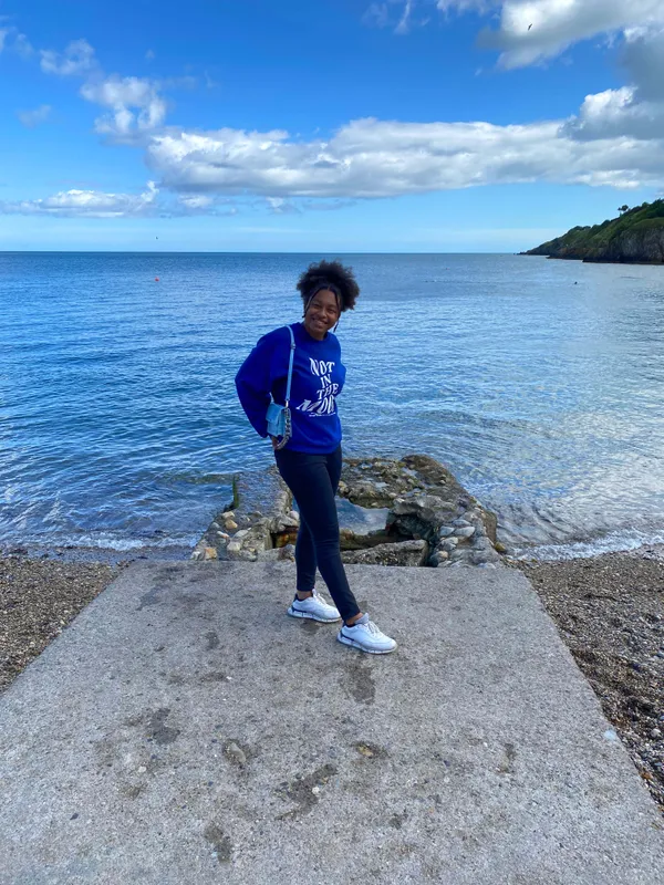 Chica posando en una rampa de hormigón junto al mar, con una colina verde al fondo