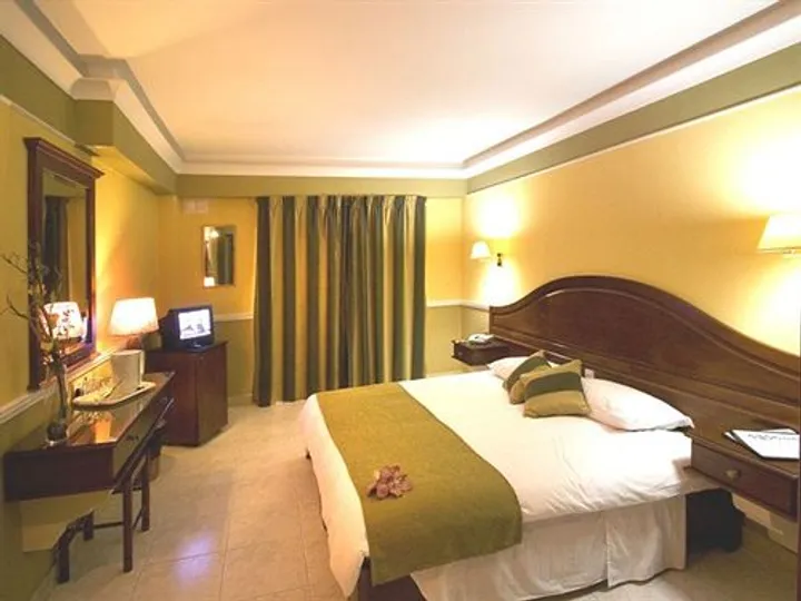 Camera dell'hotel con letto matrimoniale, testiera in legno scuro, scrivania e televisore