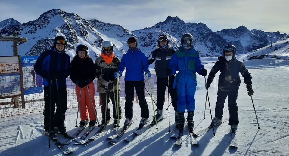 Un gruppo di persone in abiti invernali si trova su un pendio innevato con montagne innevate sullo sfondo nel terreno della Sligo Grammar School.