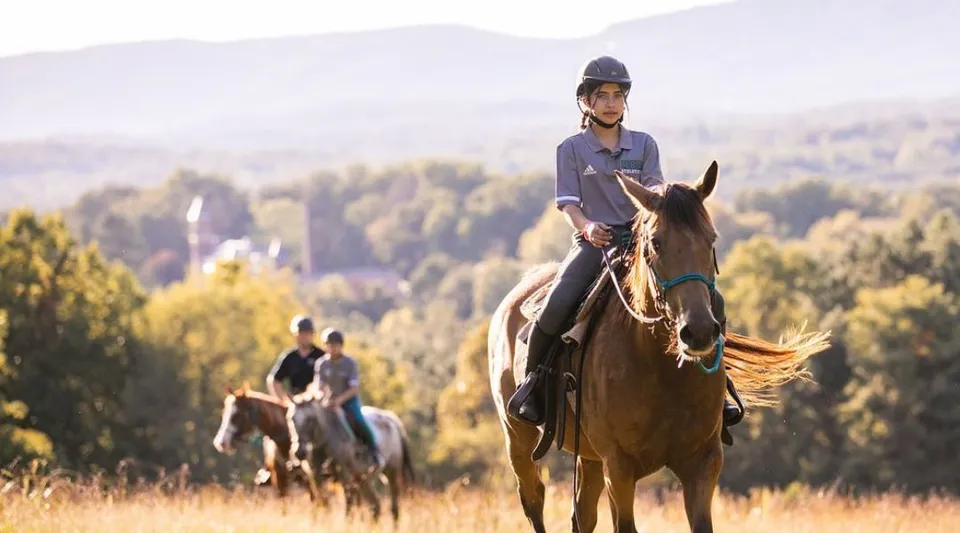 Una persona cavalca un cavallo in un paesaggio montano con boschi all'interno del campus della Miller School of Albemarle.