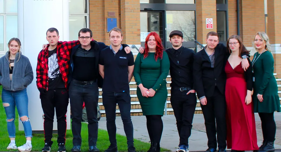 Un gruppo di studenti e studentesse sta davanti all'edificio con facciata in vetro sul campus del Weymouth College.