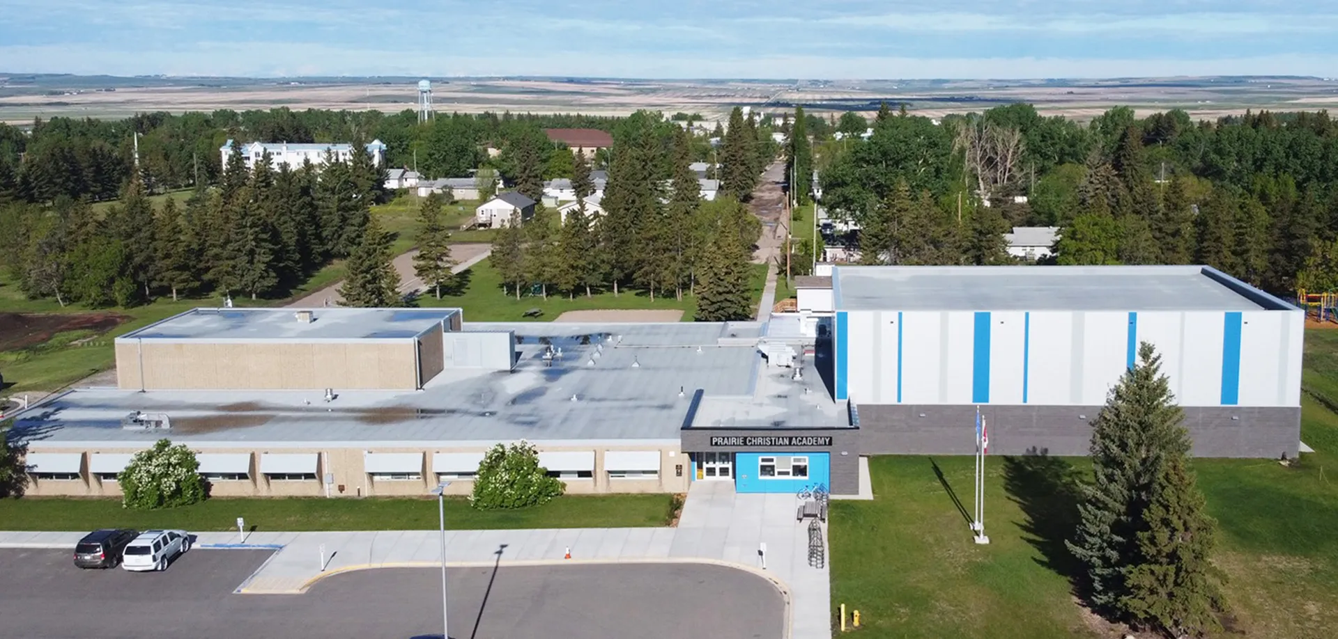 L'edificio principale moderno della Prairie Christian Academy si trova davanti a un prato con un bosco sullo sfondo, sotto un cielo azzurro.