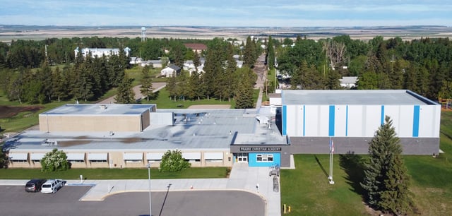 L'edificio principale moderno della Prairie Christian Academy si trova davanti a un prato con un bosco sullo sfondo, sotto un cielo azzurro.