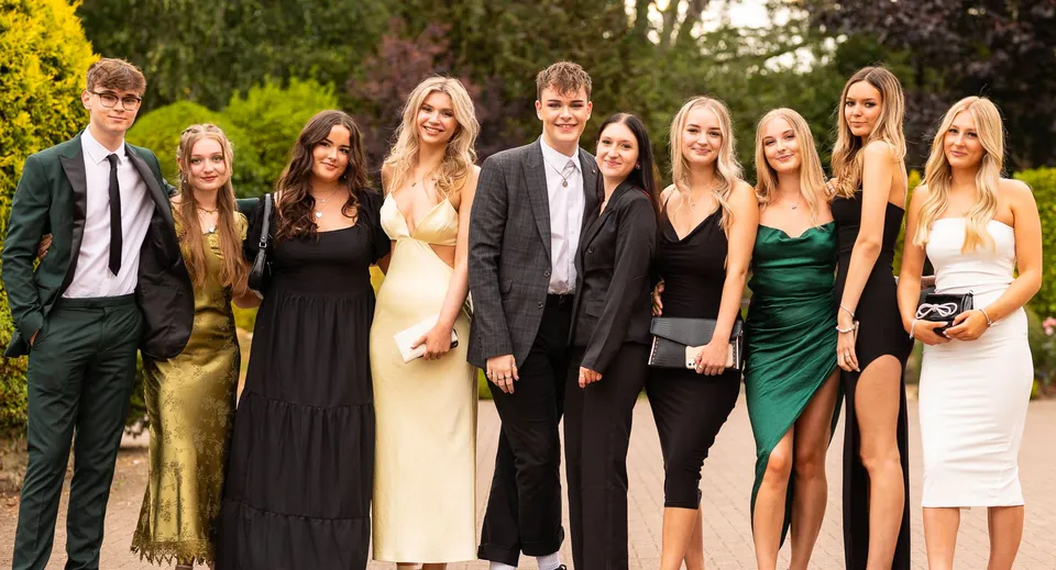 Un gruppo di studenti ben vestiti posa all'aperto sul campus del Frome College davanti ad alberi e verde.