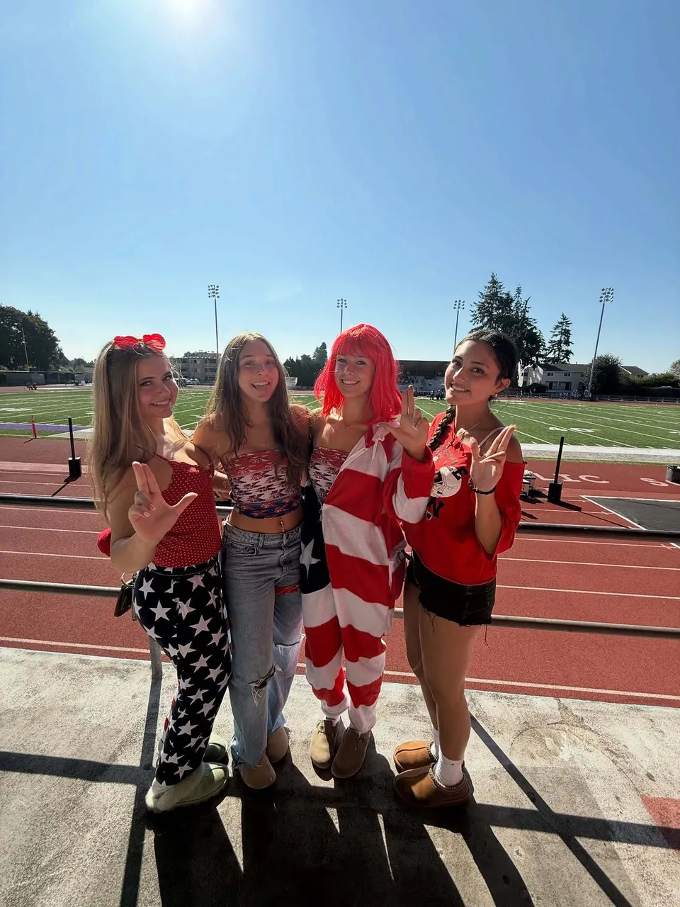 Quattro studentesse della Kennedy Catholic High School si mettono in posa con abiti patriottici su un campo sportivo con lo stadio sullo sfondo.