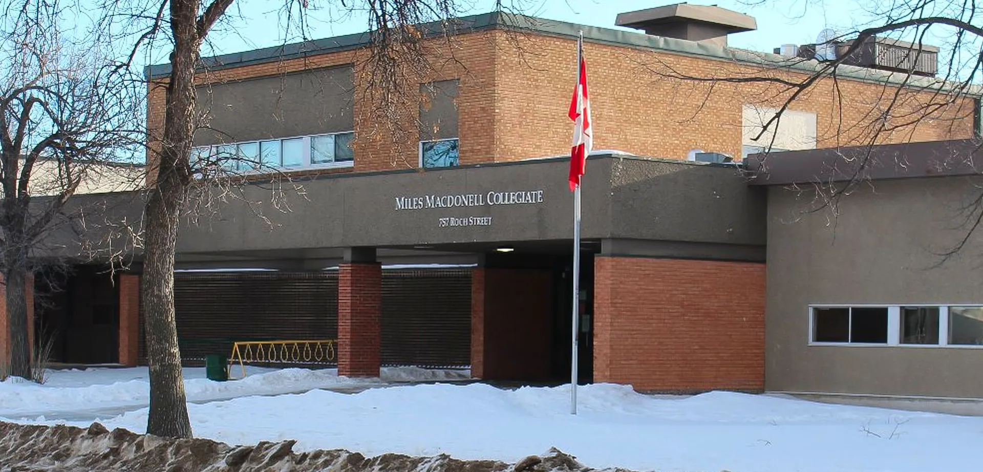 L'edificio in mattoni con la bandiera canadese si trova sul terreno innevato del Miles Macdonell Collegiate.