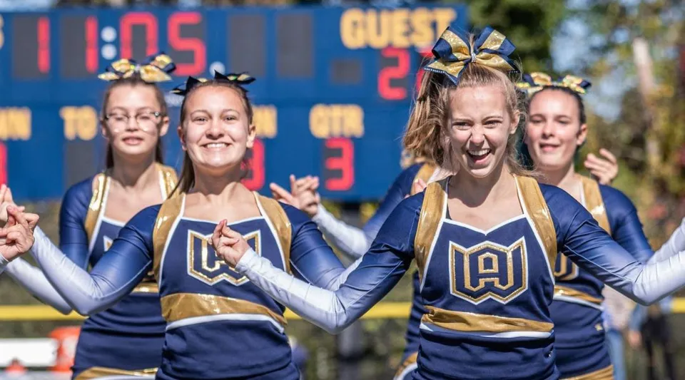 Studentesse della Woodstock Academy in uniforme da cheerleader stanno davanti a un tabellone segnapunti.