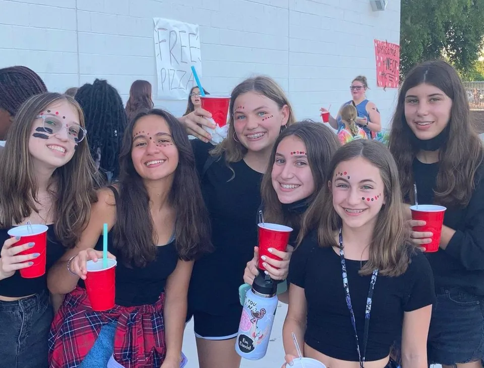 Un gruppo di giovani donne della Williams Field High School è in piedi insieme con bicchieri rossi in mano.