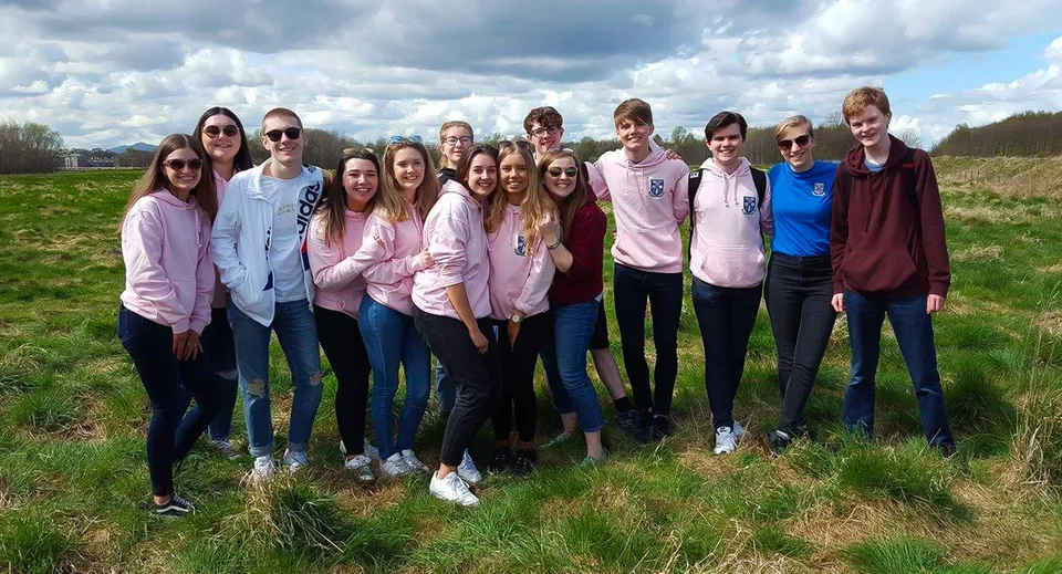 Un gruppo di studenti e studentesse si trova su un prato sotto un cielo nuvoloso nel terreno della Musselburgh Grammar School.