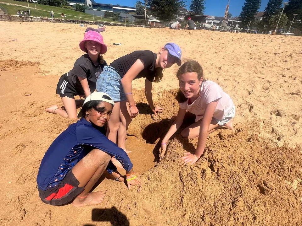 Quattro studentesse della Riverside Girls High School scavano una buca nella sabbia sulla spiaggia.