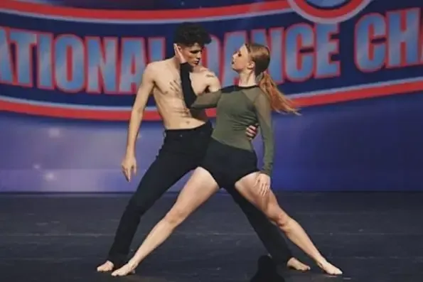 Dos jóvenes realizan una coreografía de baile en un escenario ante un gran cartel