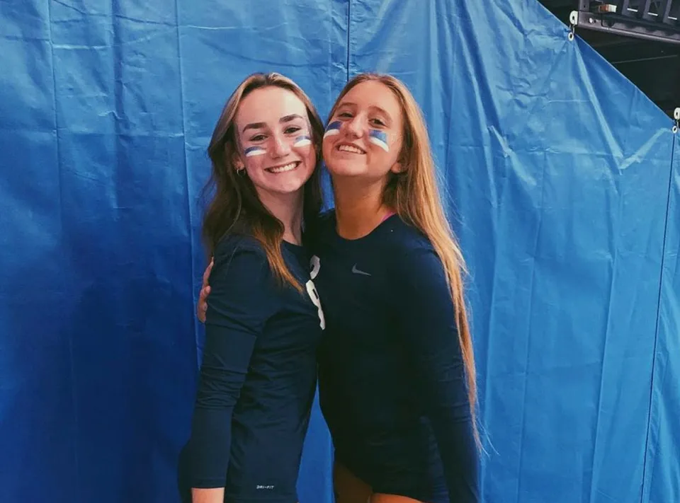Due studentesse della Lacey Township High School si abbracciano davanti a uno sfondo blu e sorridono.
