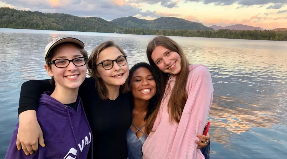 Un gruppo di studentesse della Oldfields School posa sorridendo davanti a un lago con montagne e boschi sullo sfondo.