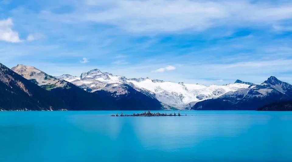Un lago limpido e turchese davanti a montagne innevate sotto un cielo blu, vicino alla St. Benedict Catholic Secondary School.