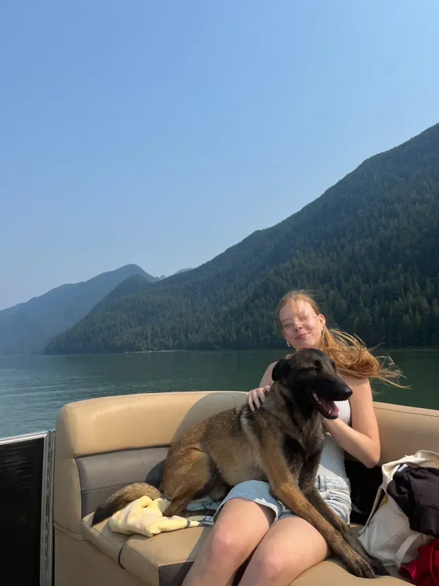 Studentessa che accarezza un cane a bordo di una barca su un lago circondato da montagne in Canada